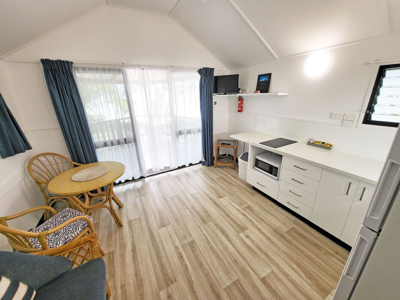 A compact kitchen with a dining area, white cabinets, a small TV, and a fire extinguisher.