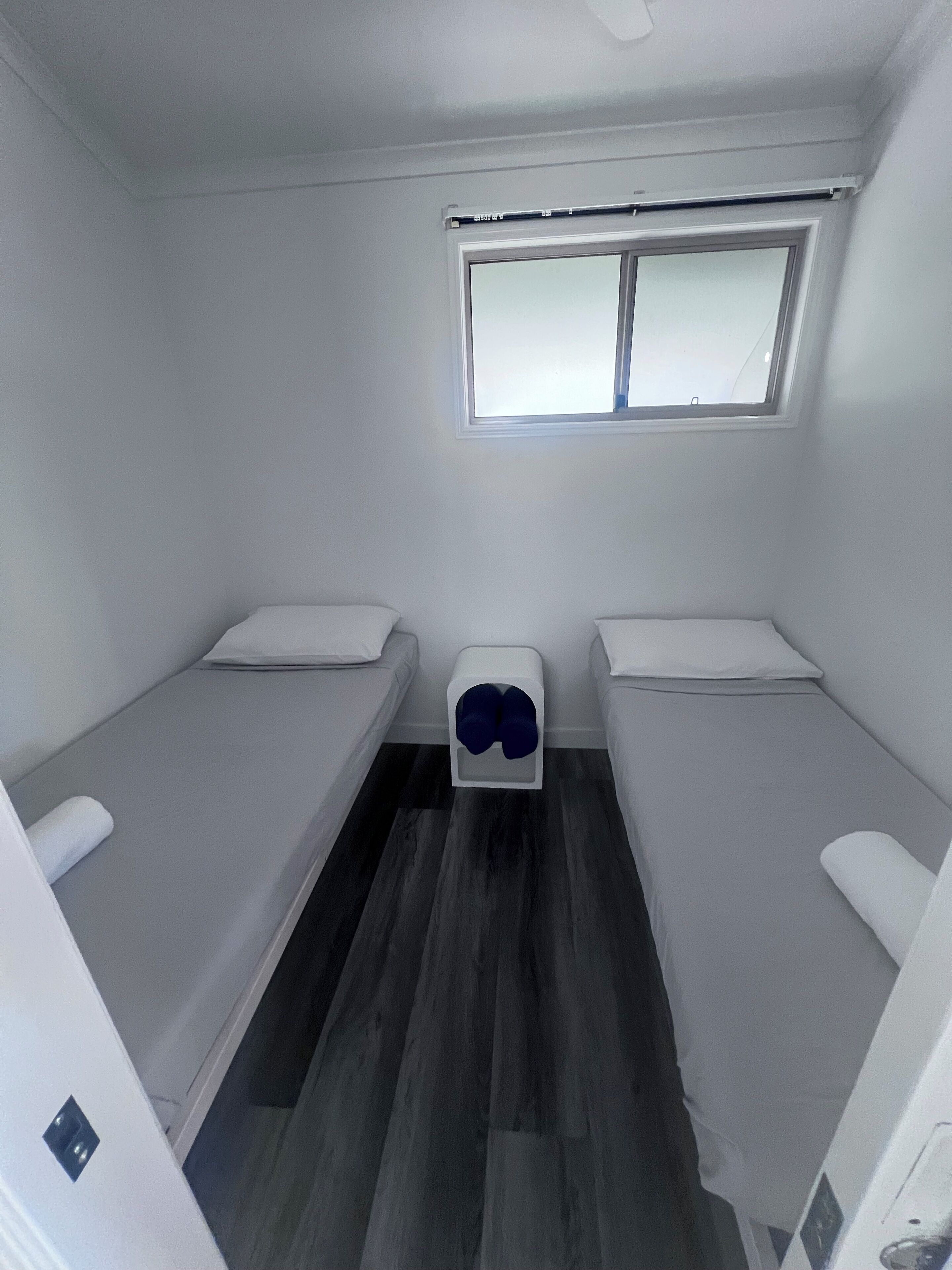 A compact room with two single beds, a small window, and a ceiling fan.