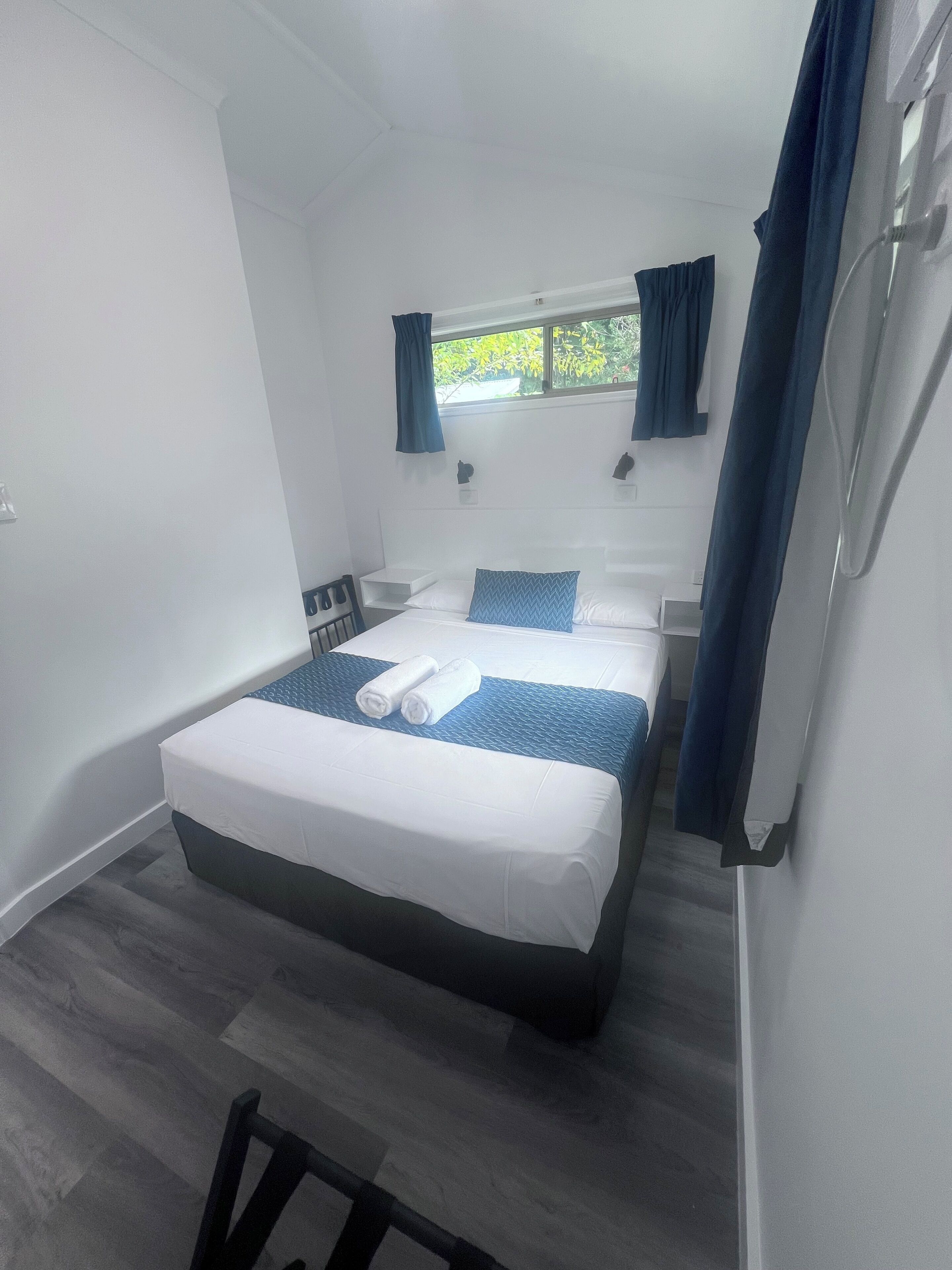 Un dormitorio pequeño y moderno con una cama individual, una mesita de noche, una ventana con cortinas y vistas a zonas verdes.