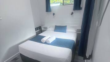 Un dormitorio pequeño y moderno con una cama individual, una mesita de noche, una ventana con cortinas y vistas a zonas verdes.