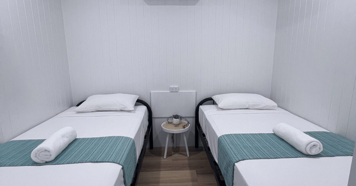 Una habitación pequeña y limpia con dos camas individuales, una mesita y un radiador.