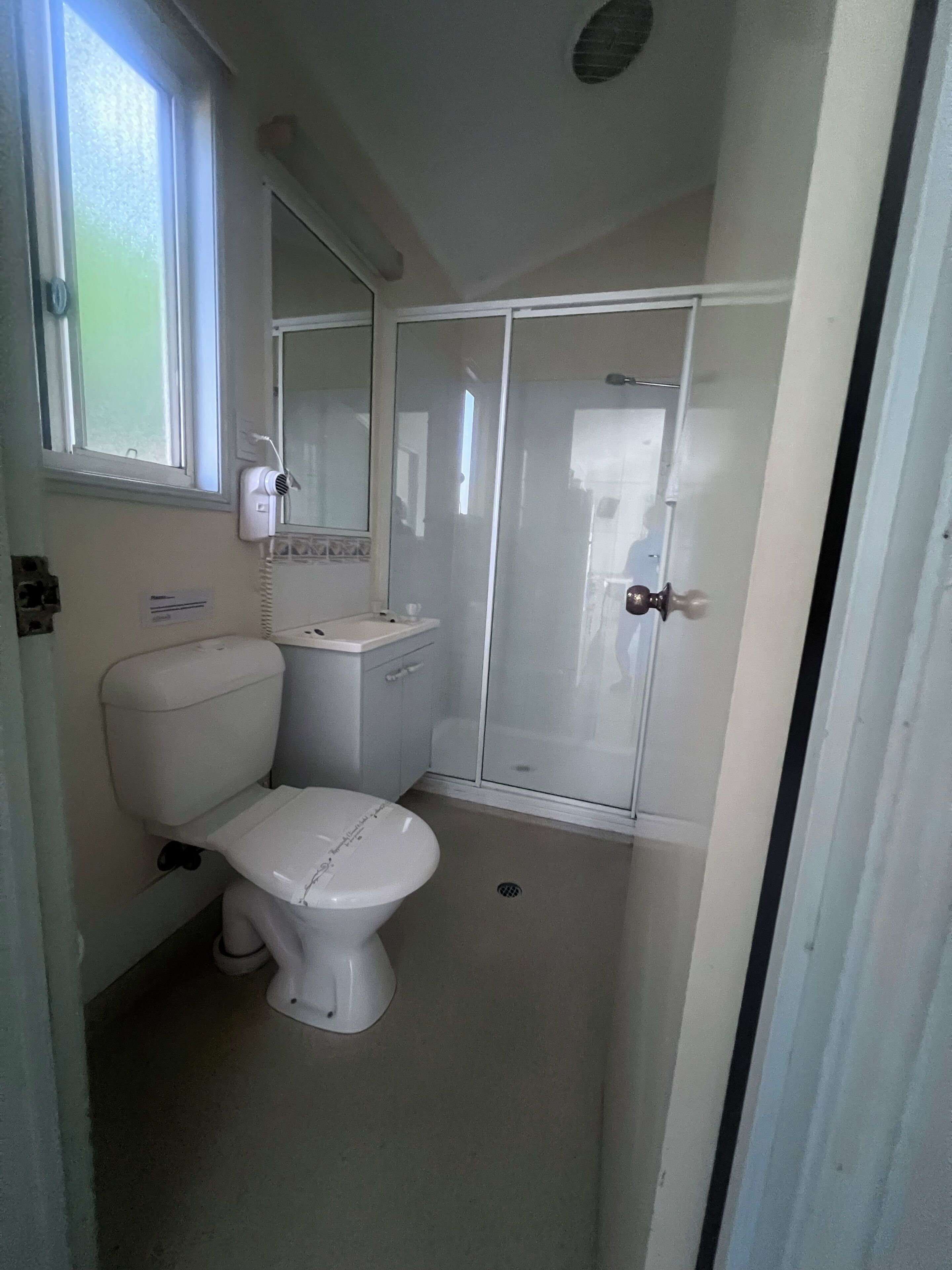 Un baño pequeño y funcional con inodoro, lavamanos y cabina de ducha de vidrio.