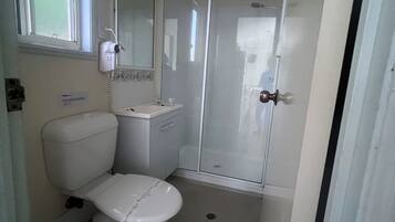 Un baño pequeño y funcional con inodoro, lavamanos y cabina de ducha de vidrio.