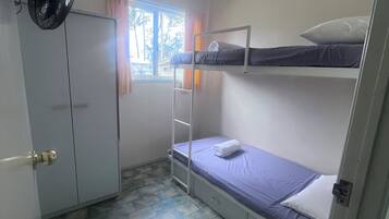 A small, compact room with a bunk bed, a wardrobe, a ceiling fan, and a window with curtains.