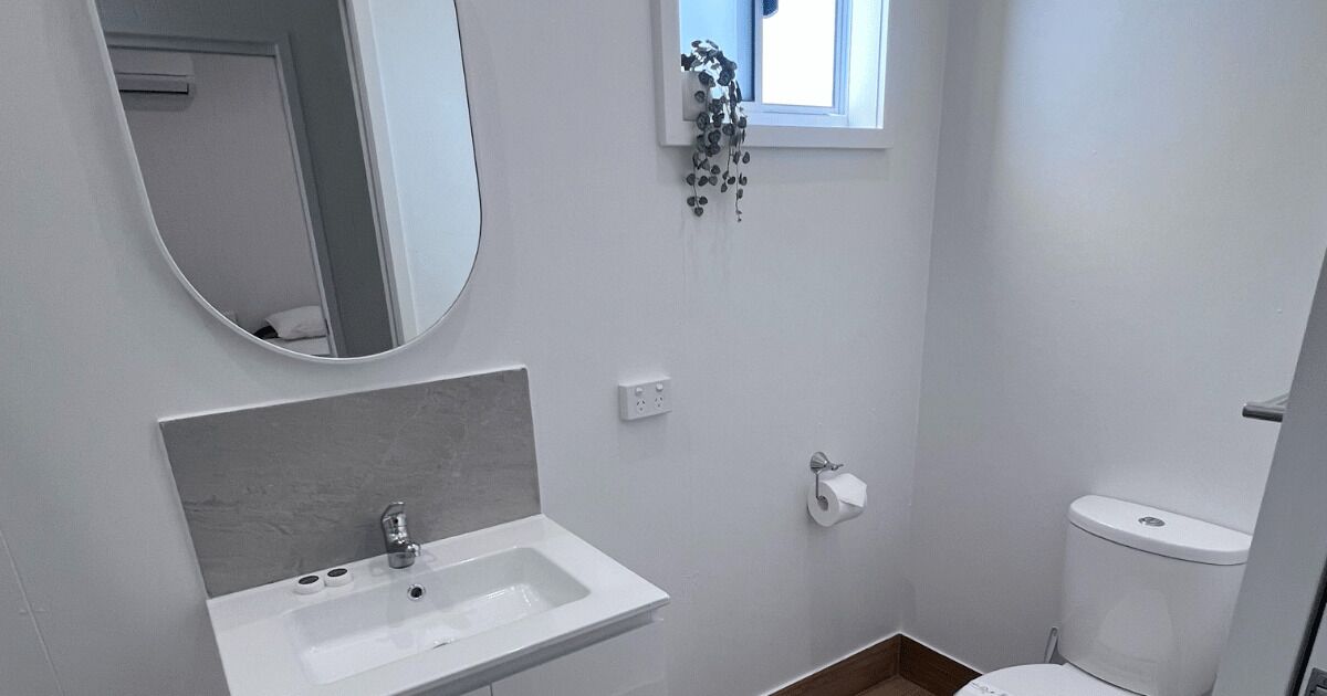 A small, modern bathroom with a white sink, mirror, and toilet.
