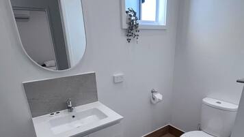 Un baño pequeño y moderno con lavamanos, espejo y retrete blancos.