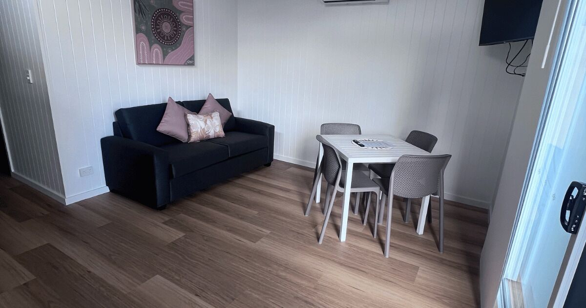 A room with a dark-colored sofa, a white table with chairs, and a wall-mounted TV.