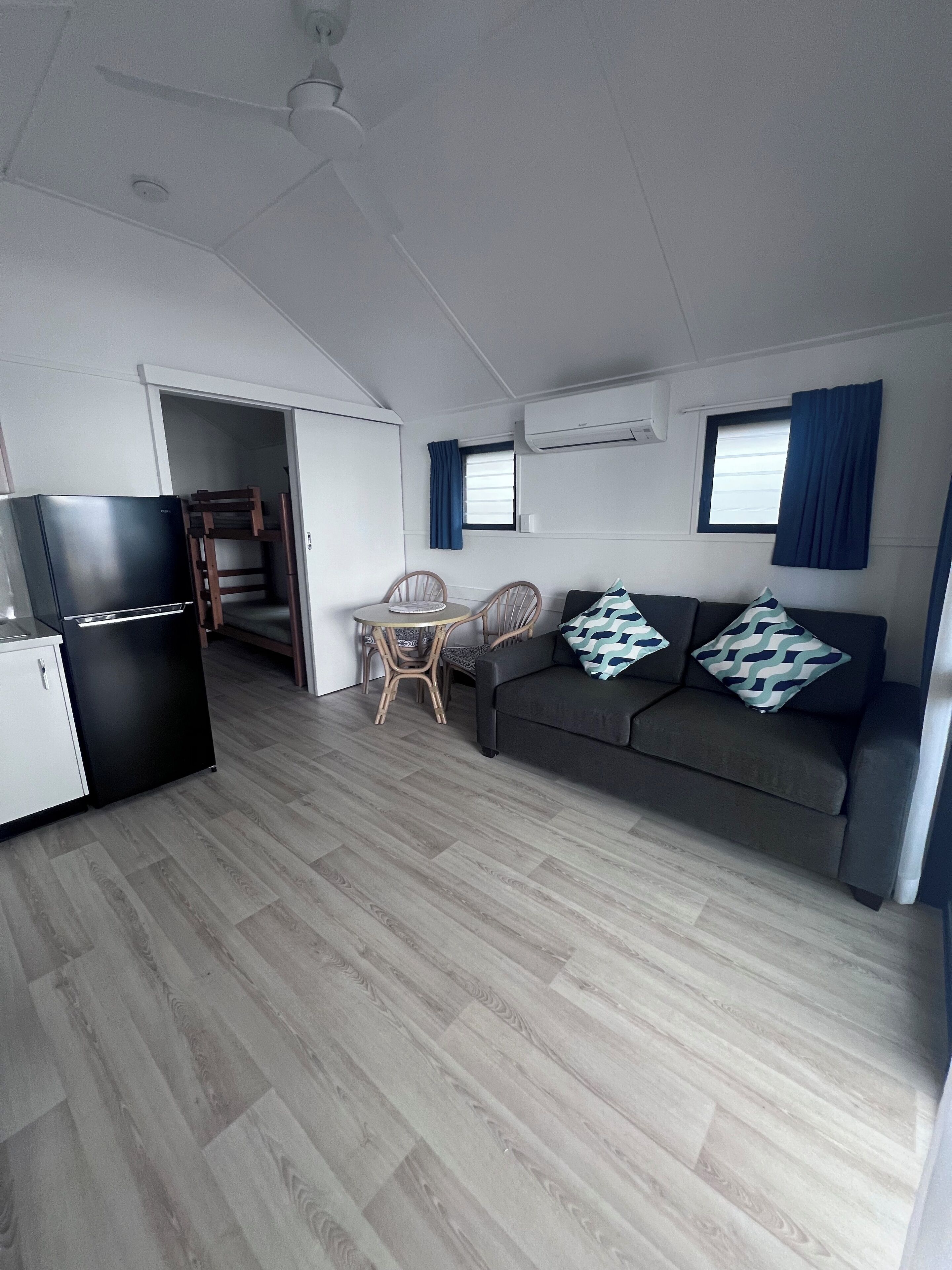 Un espace de vie compact comprenant un coin cuisine, un canapé, une table à manger avec des chaises et un ventilateur de plafond.
