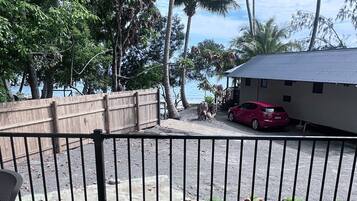 A view of a beachside property with a wooden fence, a red car, and a building with a metal roof.