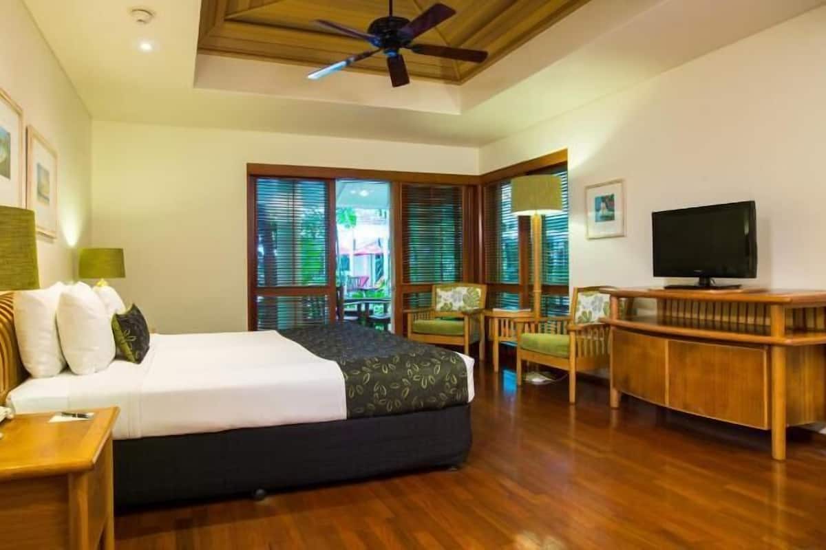 Una habitación de hotel con cama, escritorio, silla, televisor y ventilador de techo.