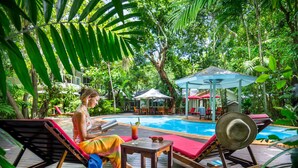 Un área junto a la piscina con sillones de descanso, una mesa y una zona de estar cubierta.
