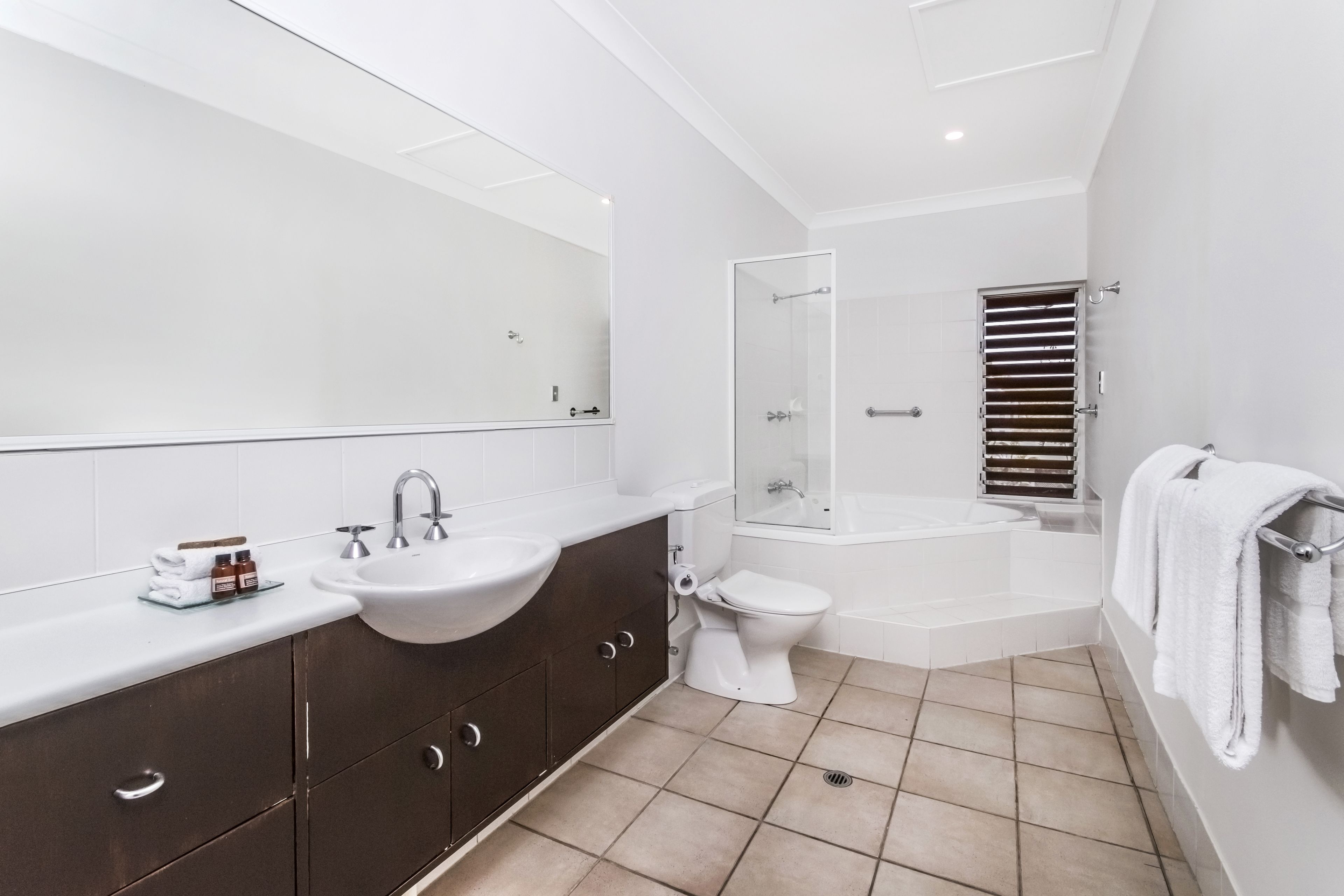 A modern bathroom with a large mirror, two sinks, a toilet, and a shower area.