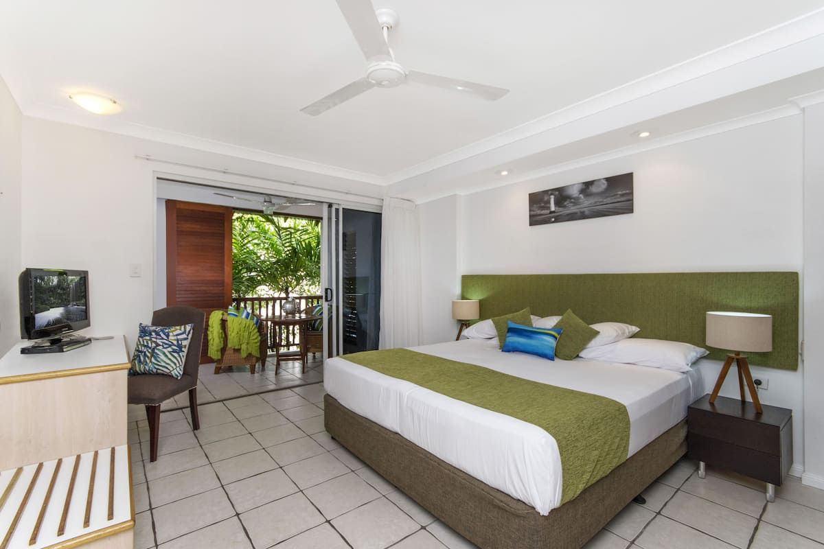 A hotel room with a bed, a desk with a computer, a chair, a balcony, and a ceiling fan.