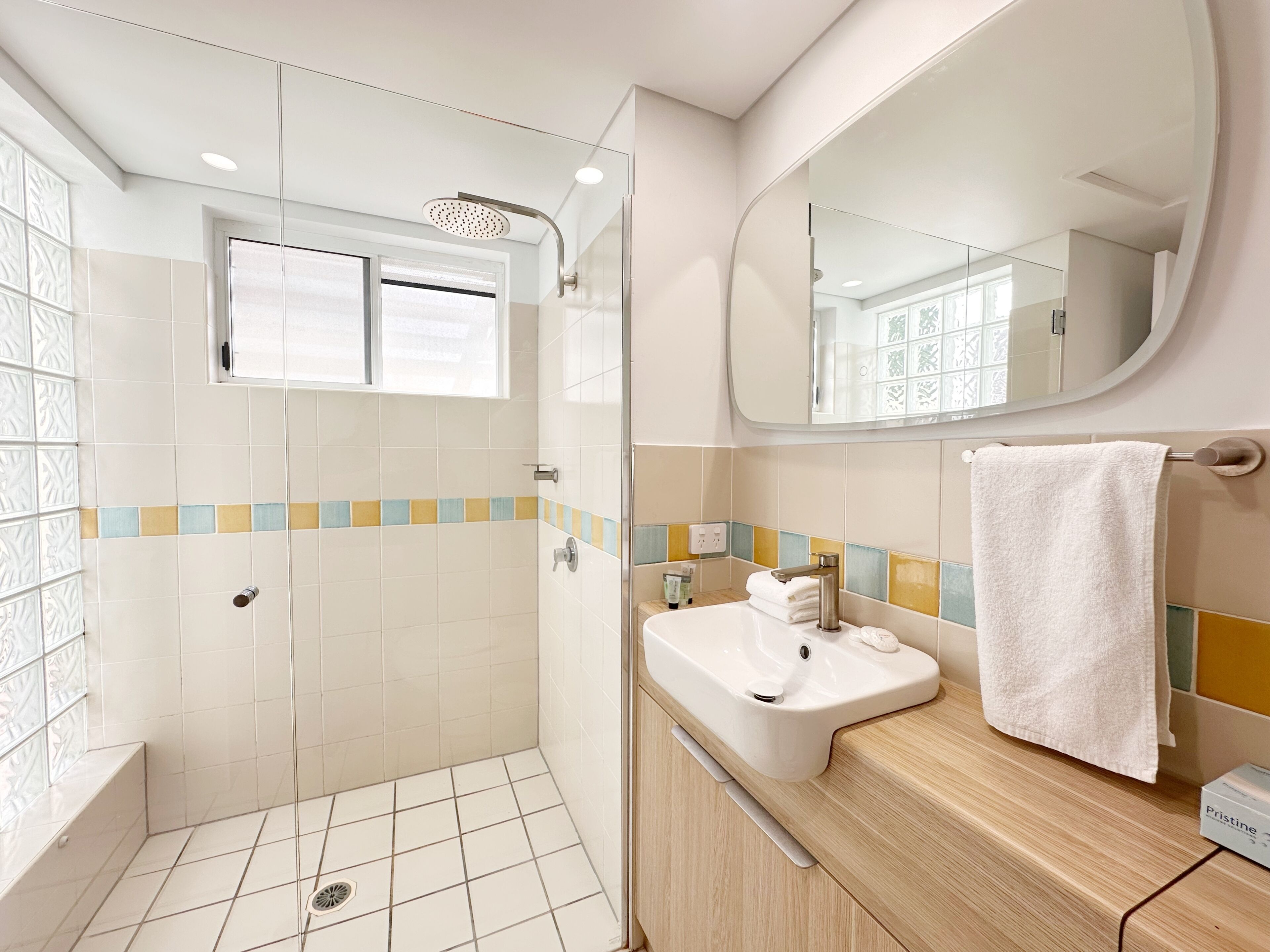 A modern bathroom with a glass shower enclosure, a white sink, a mirror, and a towel rack.