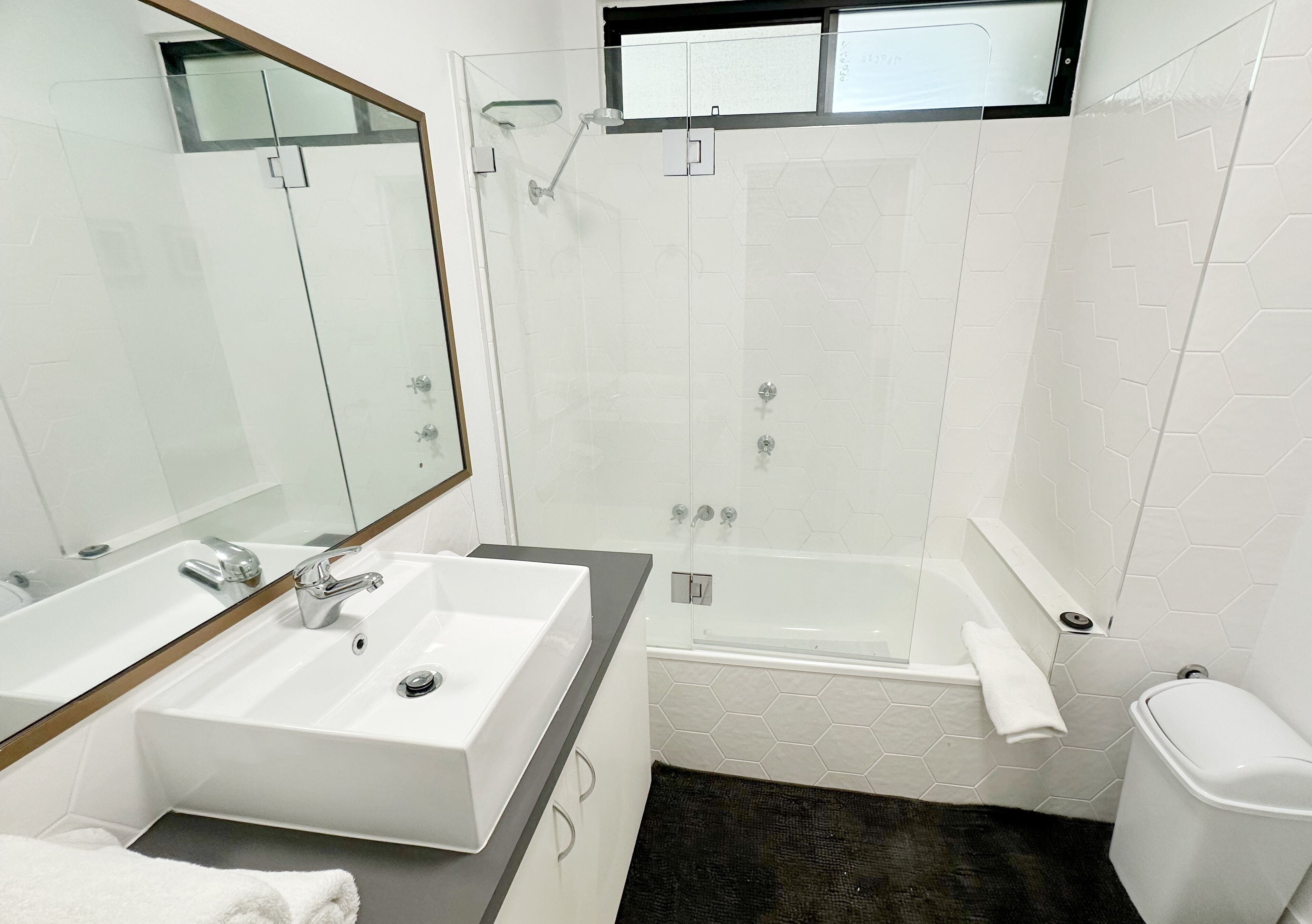A bathroom with a white sink, mirror, shower, and toilet.