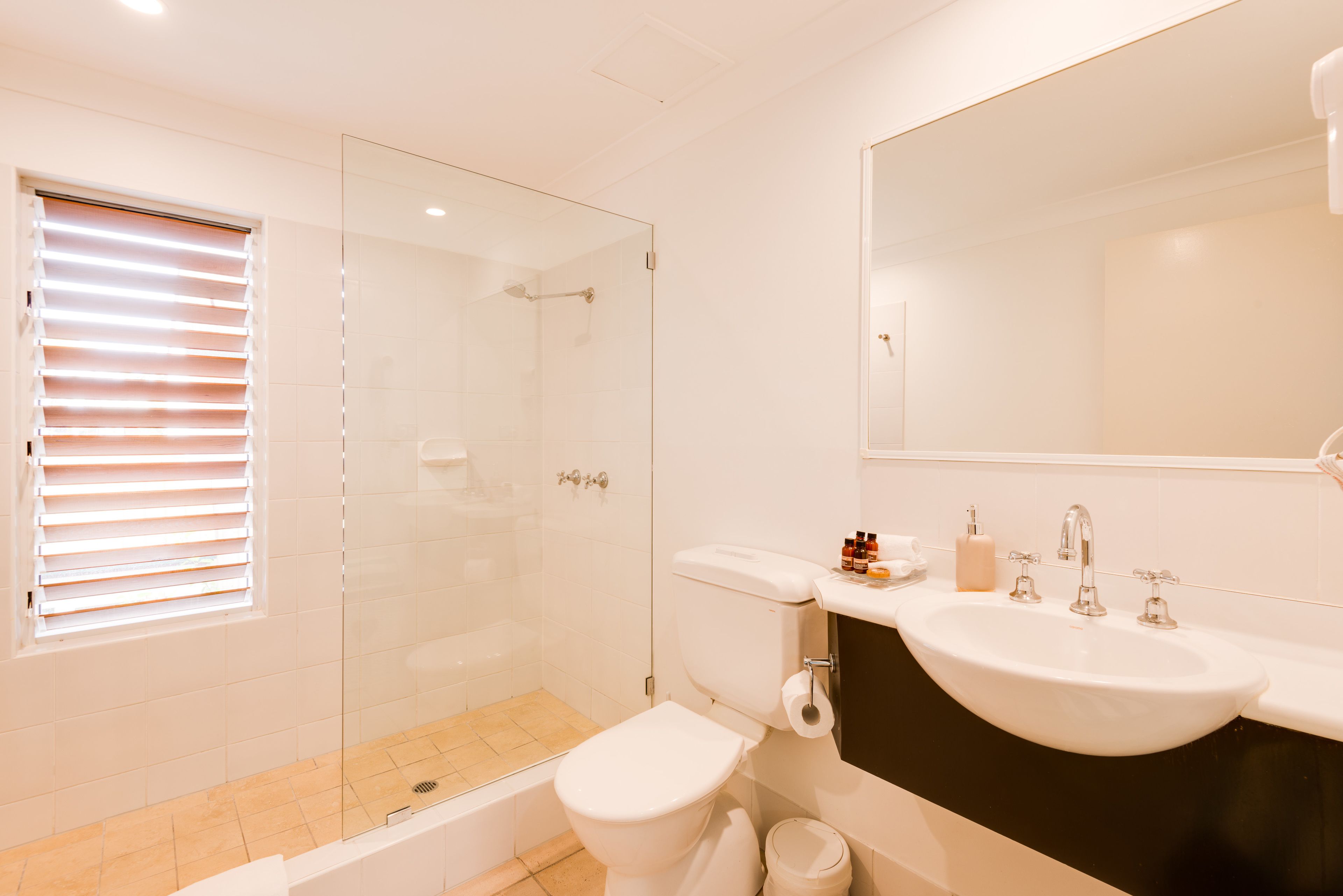 A bathroom with a glass-enclosed shower, a toilet, a sink, and a mirror.