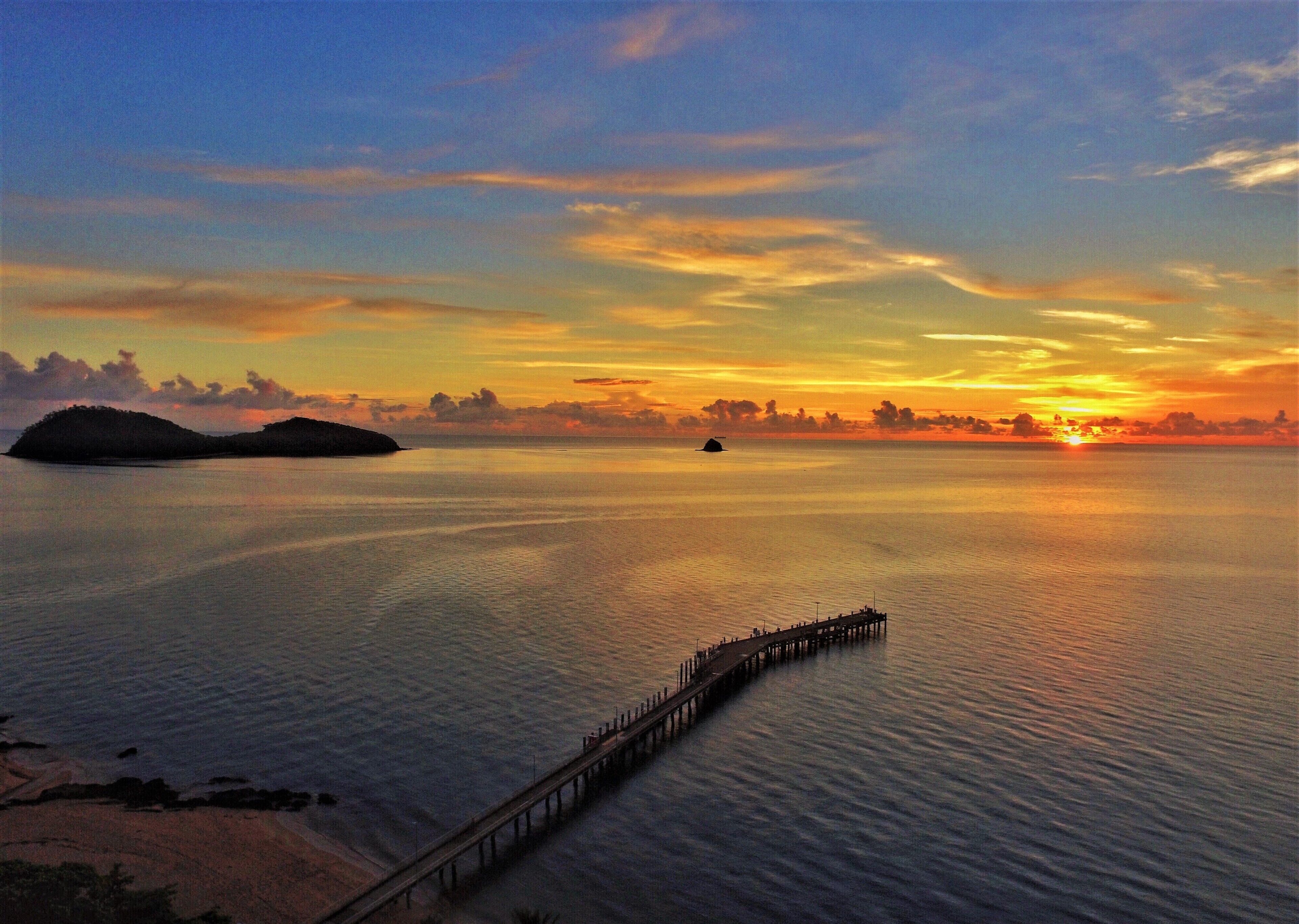 A sunset over a calm sea with a pier extending into the water.