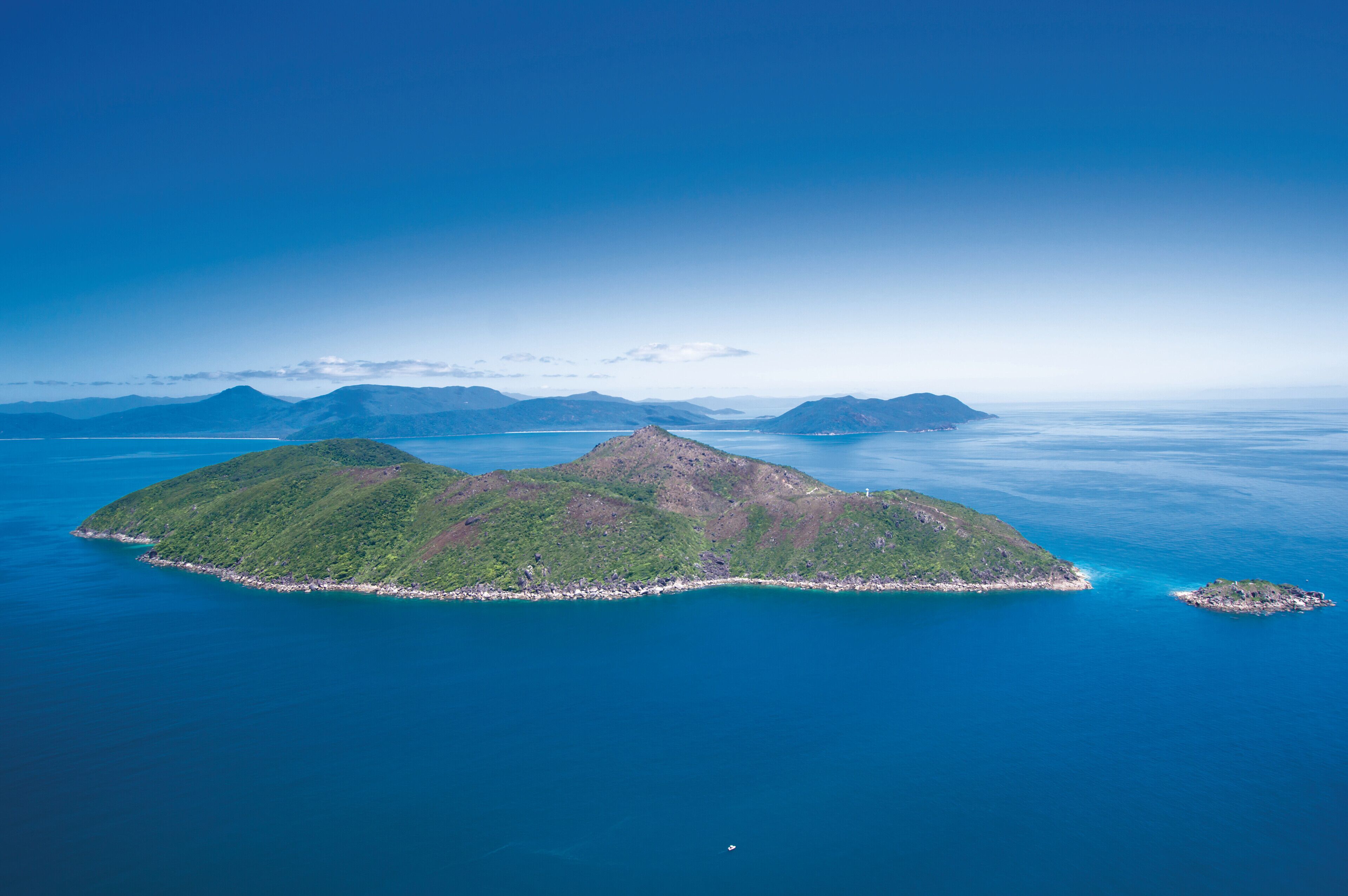 Vue aérienne d’une île tropicale, avec ses collines verdoyantes, ses eaux d’un bleu limpide et une petite plage.