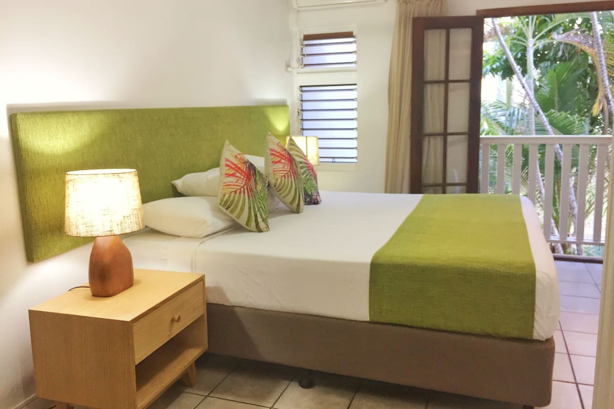 A neatly made bed with a green headboard, a bedside lamp, and decorative pillows.