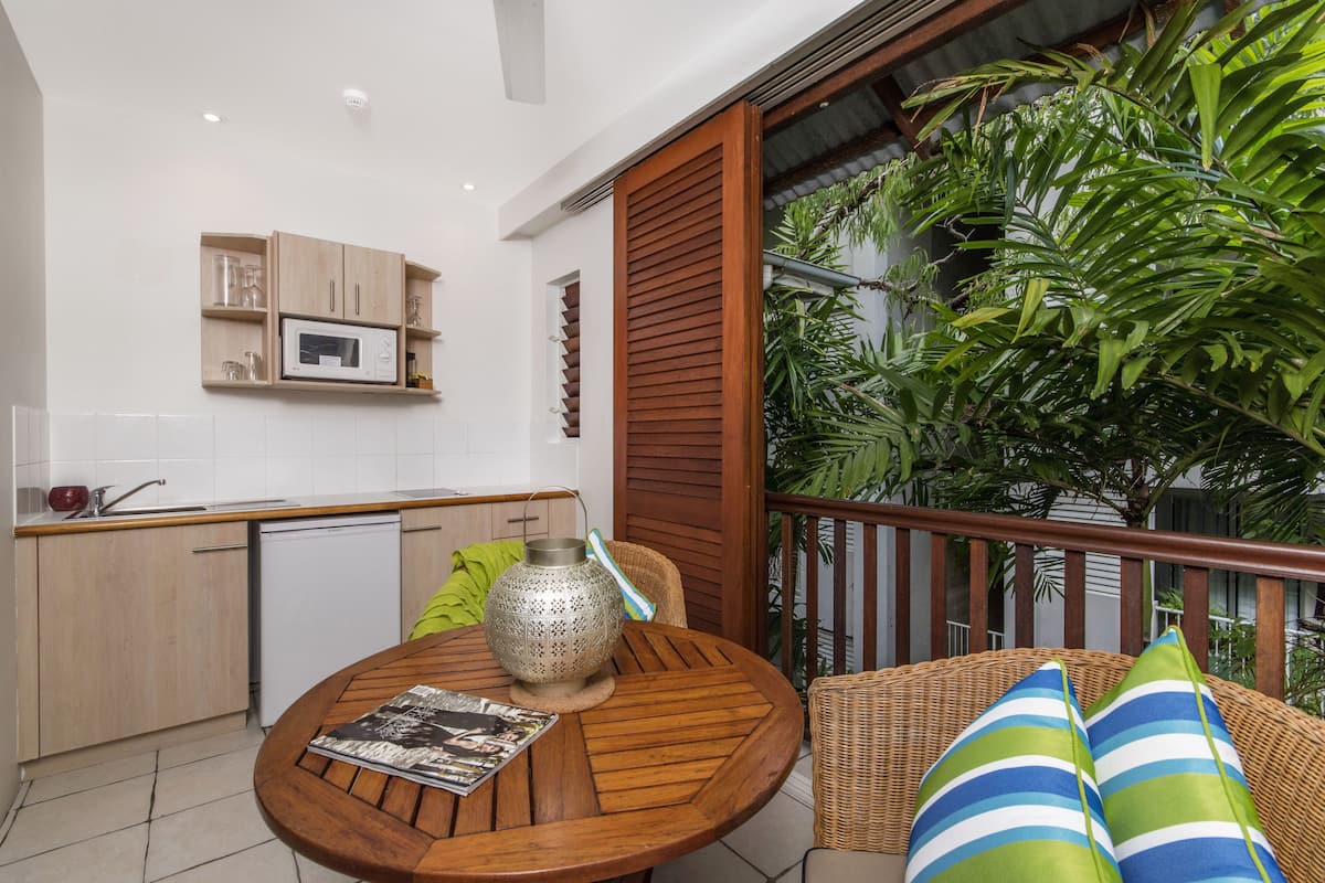 A compact kitchen with a microwave, wooden cabinets, and a dining area with a round table and wicker chair.