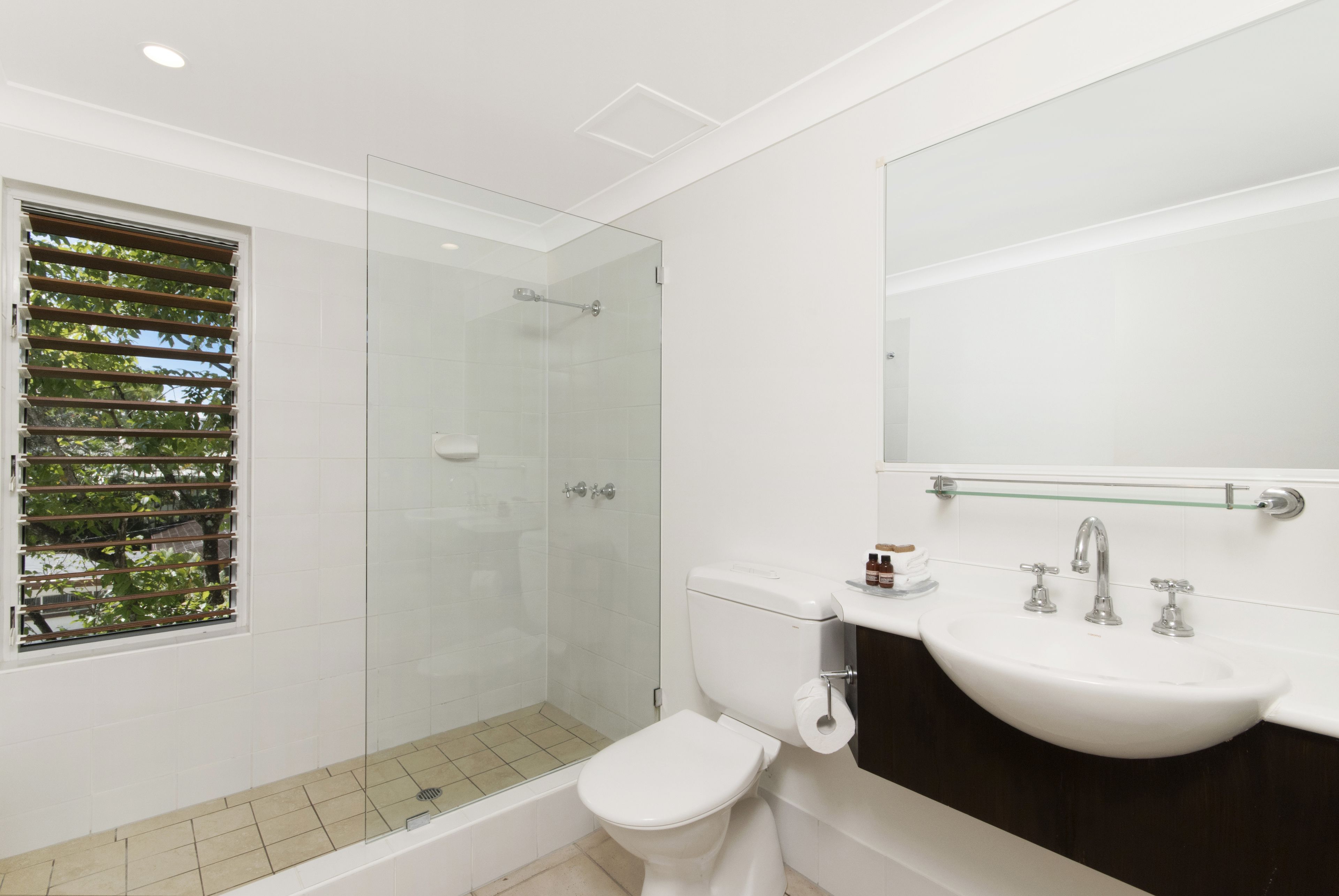 Un baño moderno con ducha de vidrio, inodoro blanco y lavamanos con espejo.