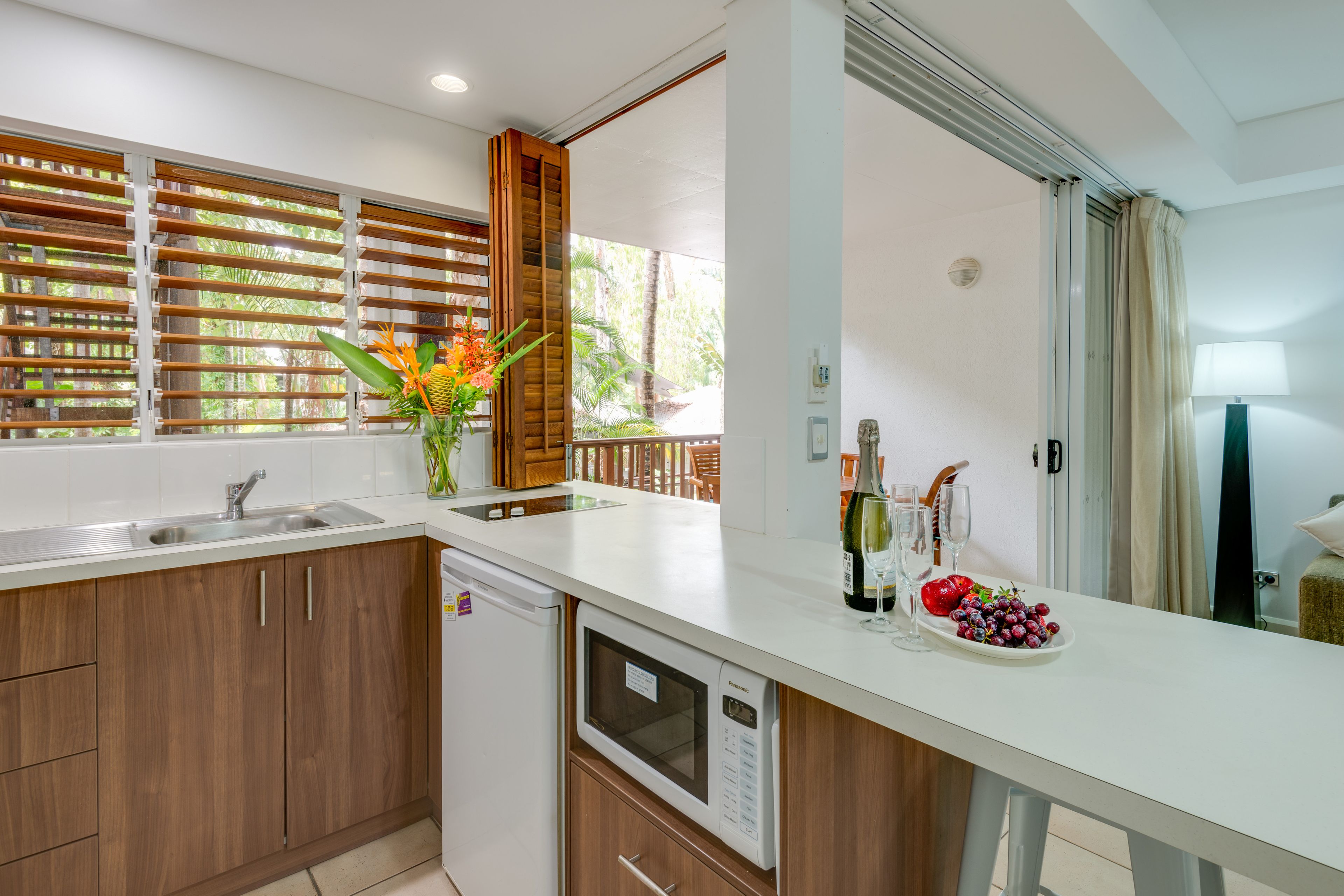 Une cuisine moderne avec des meubles en bois, un lave-vaisselle encastré et une grande fenêtre équipée de stores.