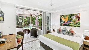 A modern hotel room with a large bed, a desk with a telephone, a chair, and a balcony with a table and chairs. - The Reef Retreat (Palm Cove)