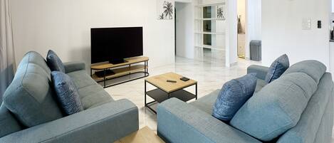 A modern living room with two grey sofas, a wooden coffee table, and a flat-screen TV.