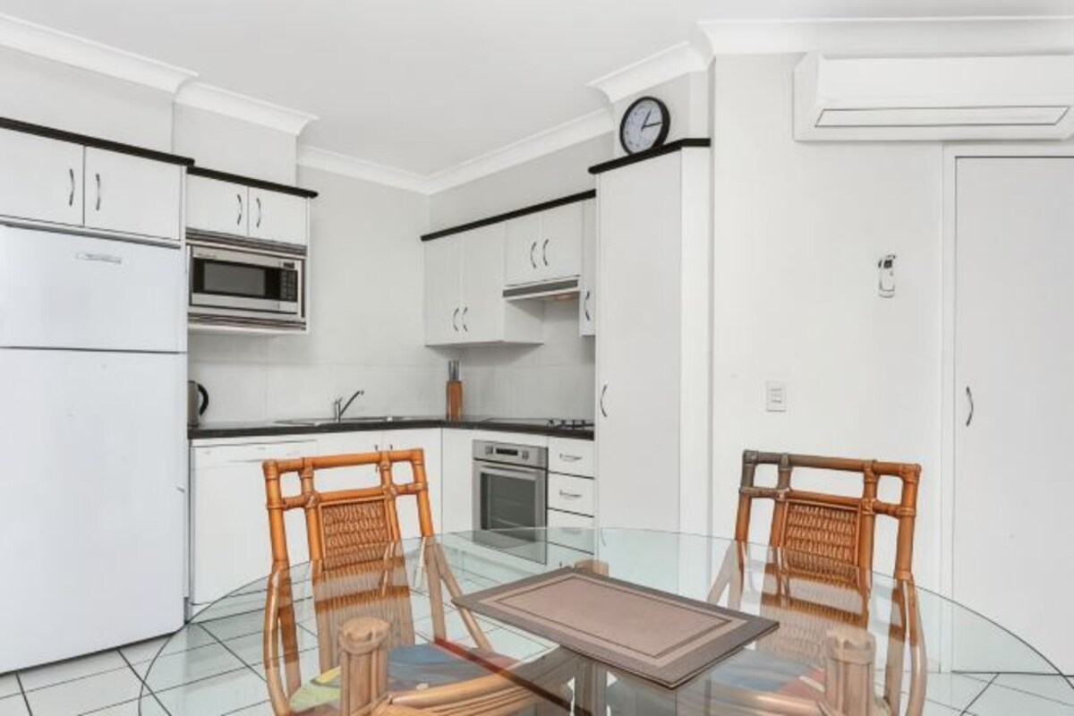 A kitchen with white cabinets, a microwave, oven, and a dining area with a glass table and wicker chairs.