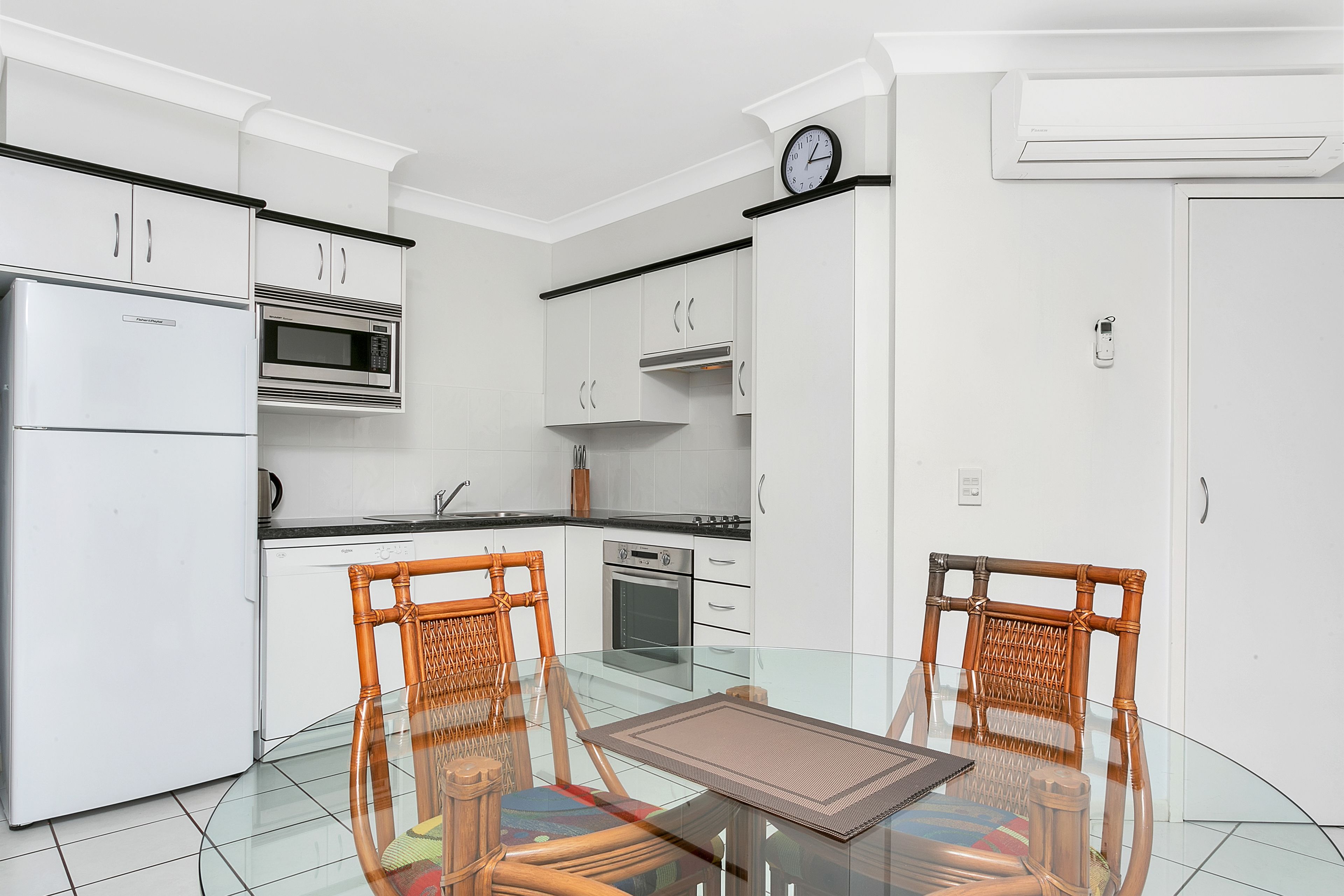 A modern kitchen with white cabinetry, a microwave, an oven, and a clock on the wall.