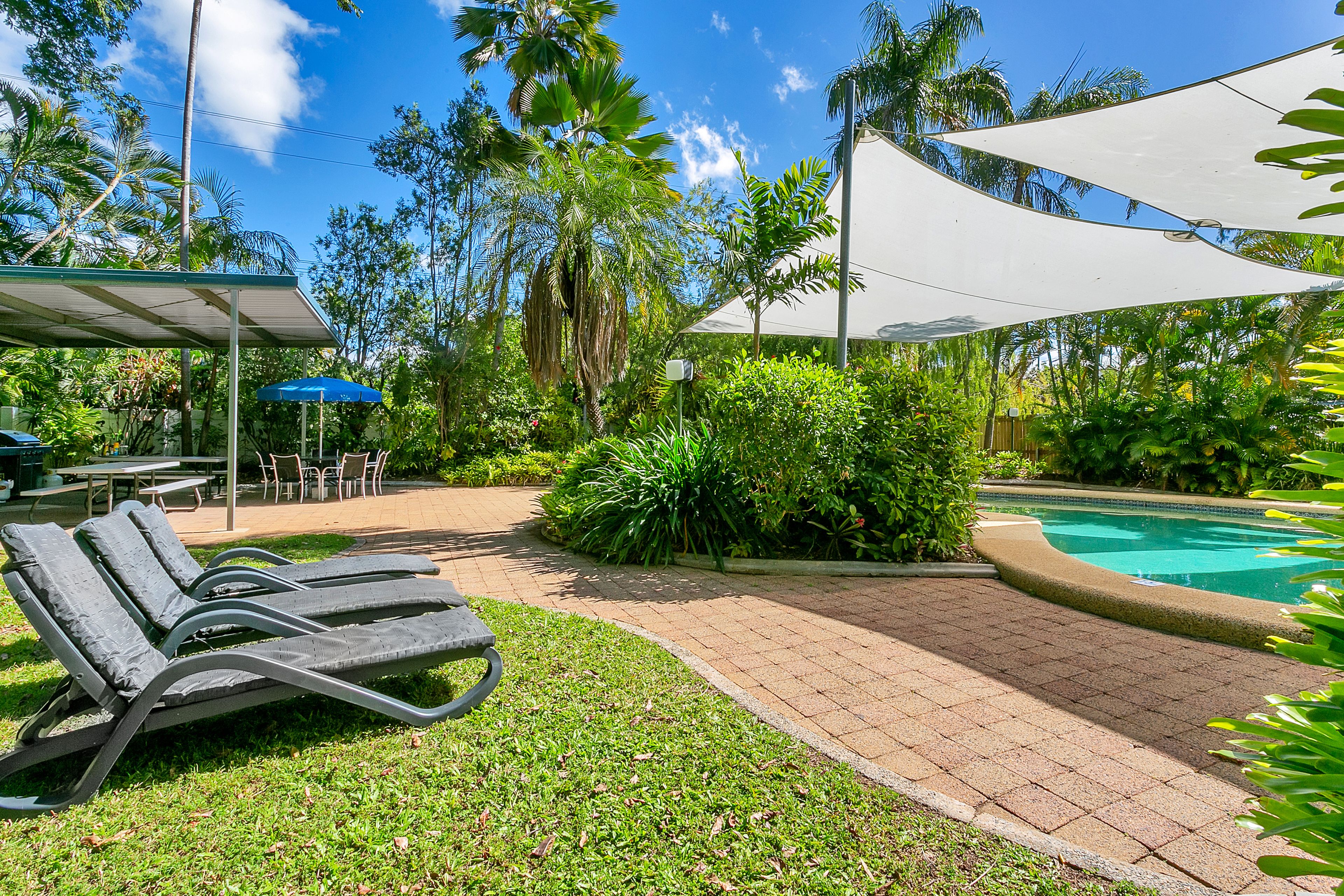 A poolside area with lounge chairs, a covered seating area, and a swimming pool surrounded by lush greenery.
