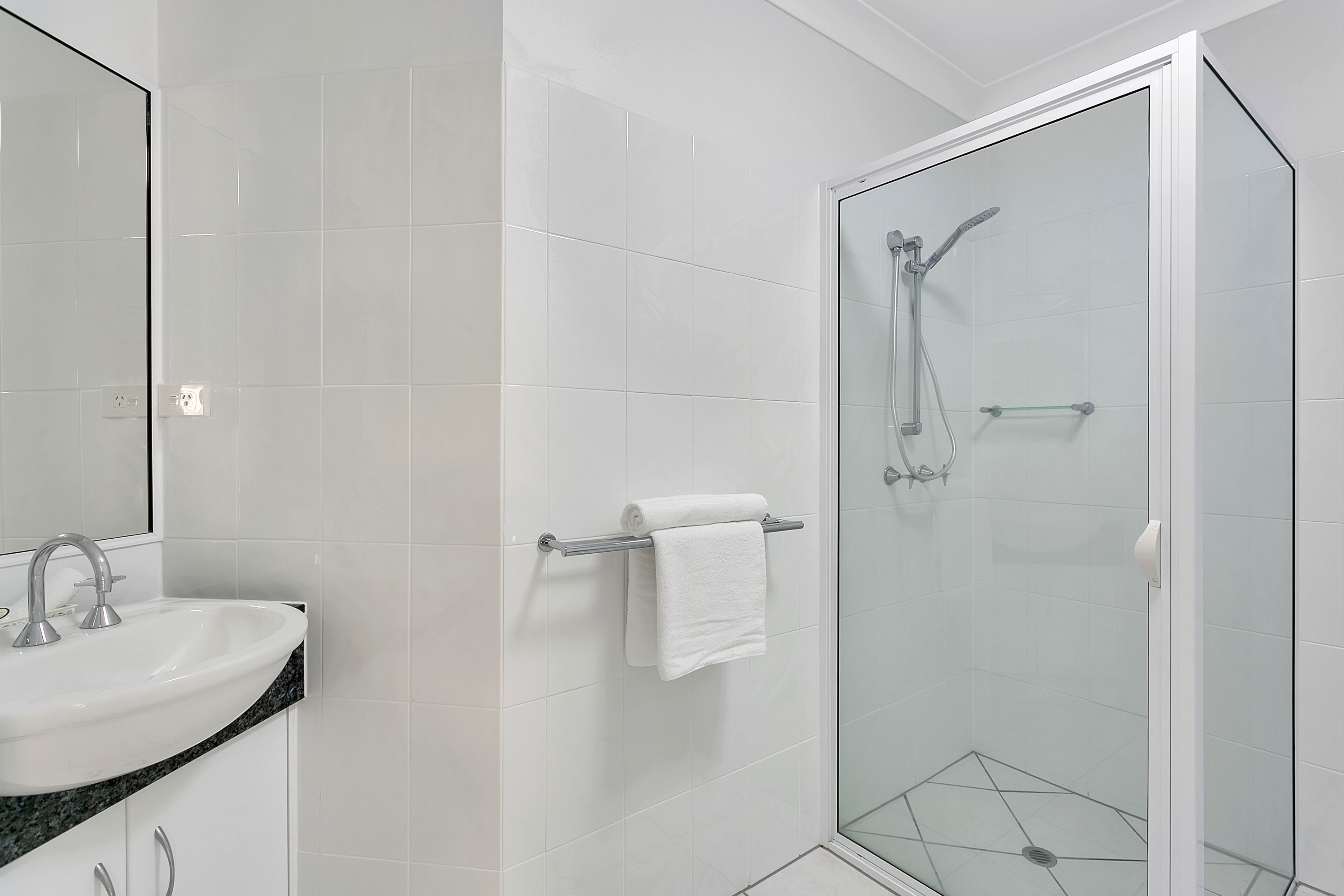 Un baño moderno con cabina de ducha de vidrio, un lavabo blanco y un perchero para toallas.