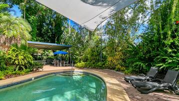 A swimming pool with lounge chairs and a covered patio area surrounded by lush greenery.