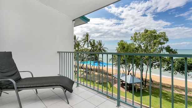 A balcony with a chair, a view of the beach, and a pool area. - Beachfront Apartments on Trinity Beach (Trinity Beach)