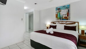 A hotel room with a large bed, a painting on the wall, and a ceiling fan. - Beachfront Apartments on Trinity Beach (Trinity Beach)