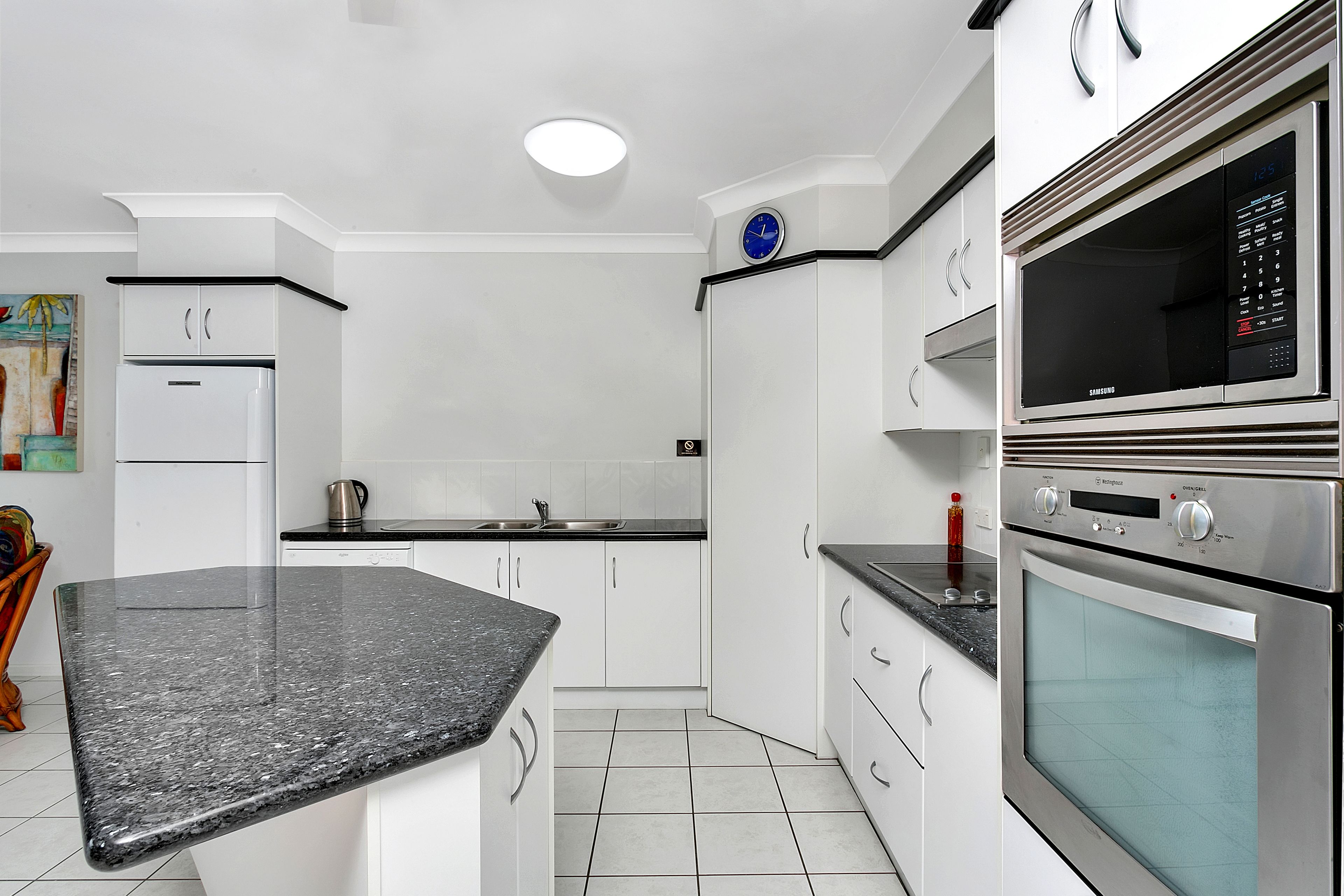 Una cocina moderna con armarios blancos, encimera de granito, electrodomésticos de acero inoxidable y un reloj en la pared.