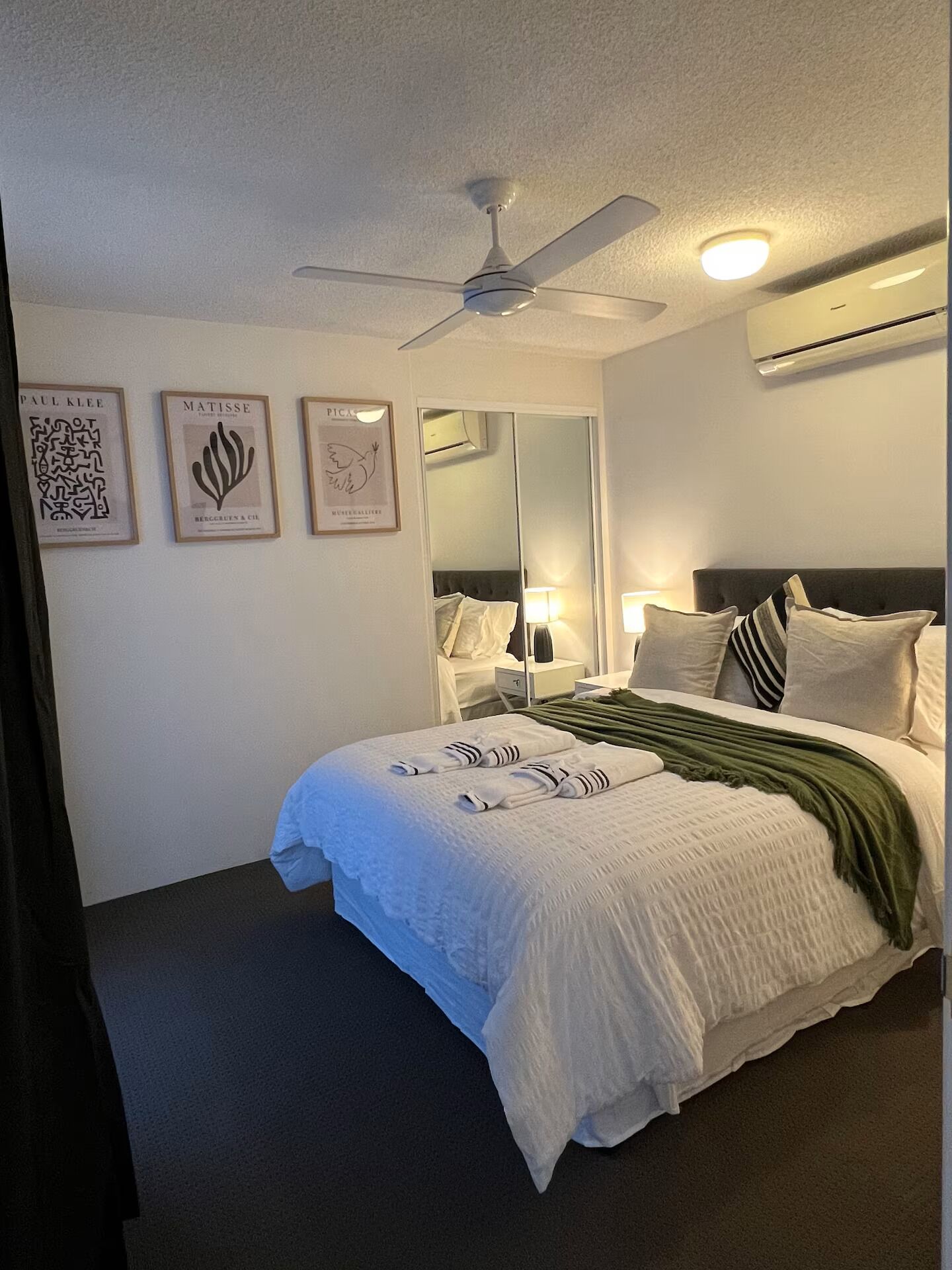 Une chambre d’hôtel avec un lit, un ventilateur de plafond, un miroir et des œuvres d’art murales.