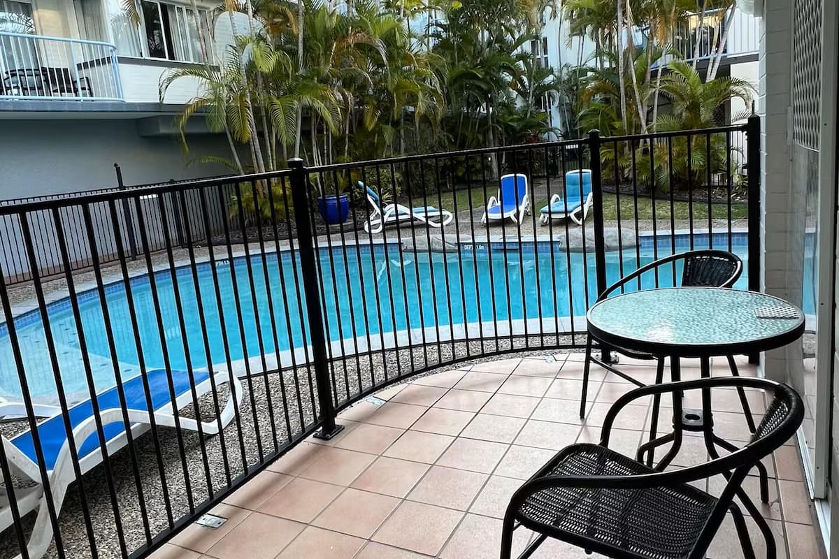 A poolside area with a tiled floor, a black metal fence, and a table with chairs.