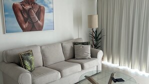 A modern living room with a beige sofa, a glass coffee table, and a ceiling fan. - Beachside Mooloolaba (Mooloolaba)