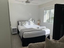 Ein Schlafzimmer mit einem Bett, einem Nachttisch, einem Deckenventilator, einem Fenster und einem Sessel.