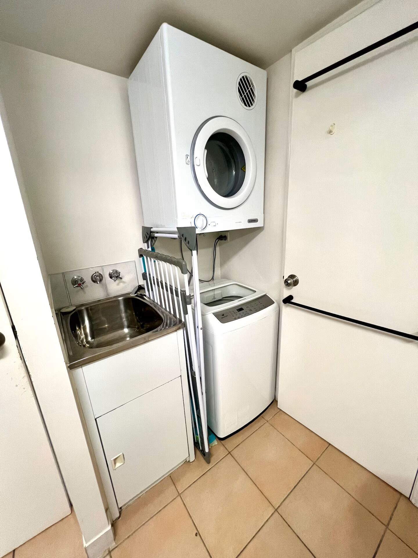 Une petite buanderie équipée d’un lave-linge, d’un évier et d’un étendoir.