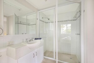 Um banheiro moderno com chuveiro em cabine de vidro, pia branca e espelho grande.