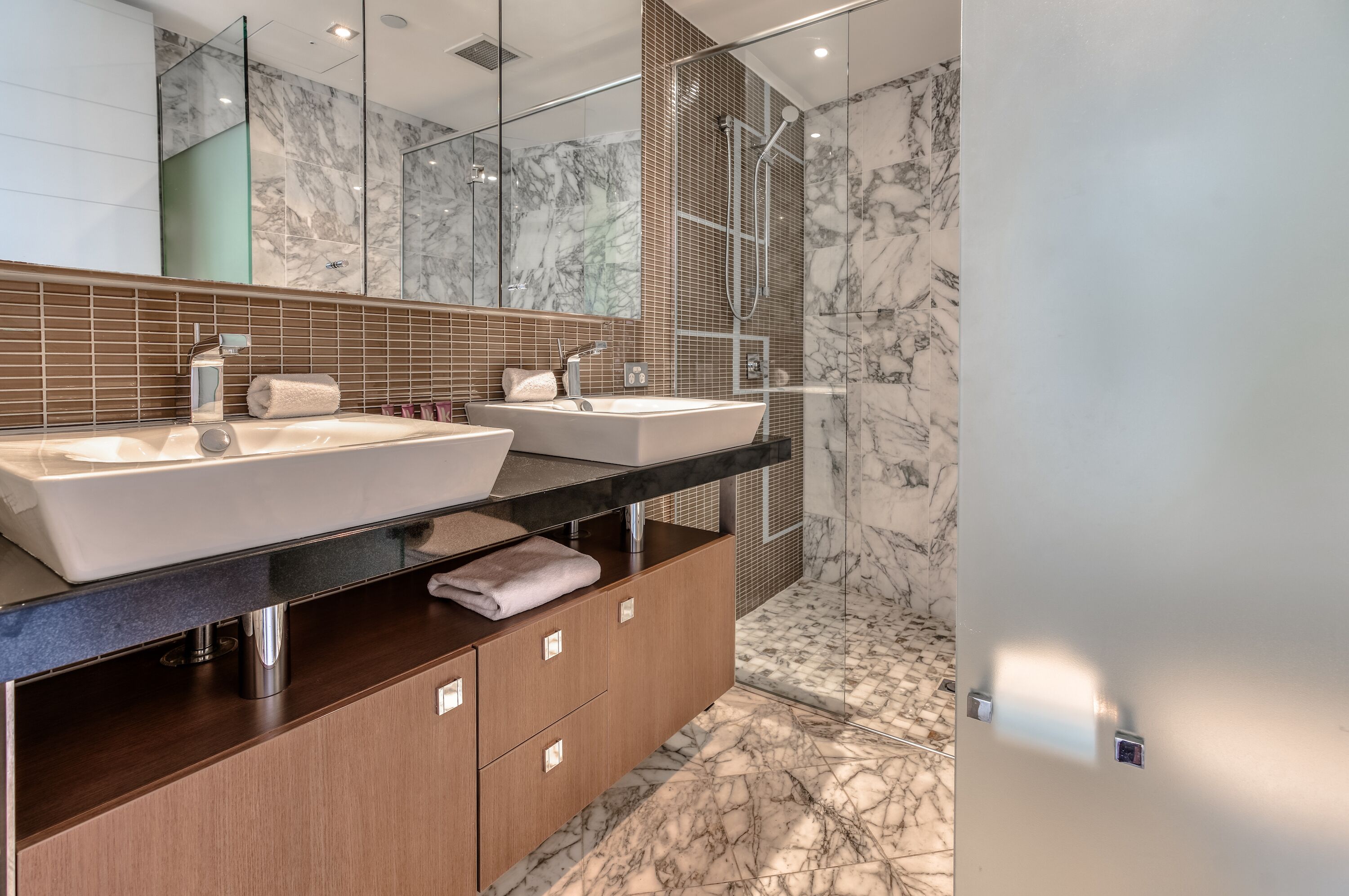 A modern bathroom with two sinks, a large mirror, and a shower area.