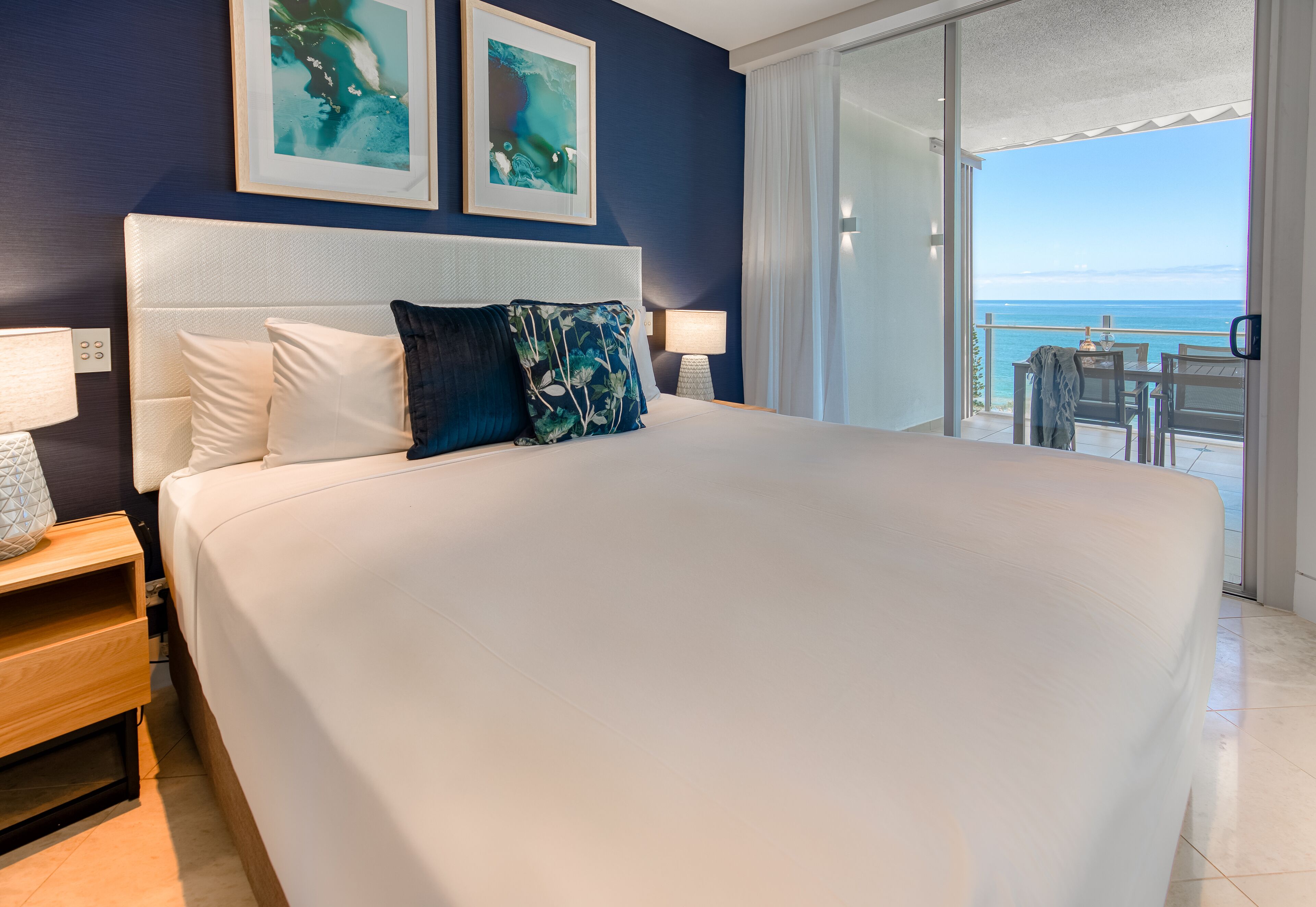 A large bed with white linens, a headboard, and two wall-mounted paintings.