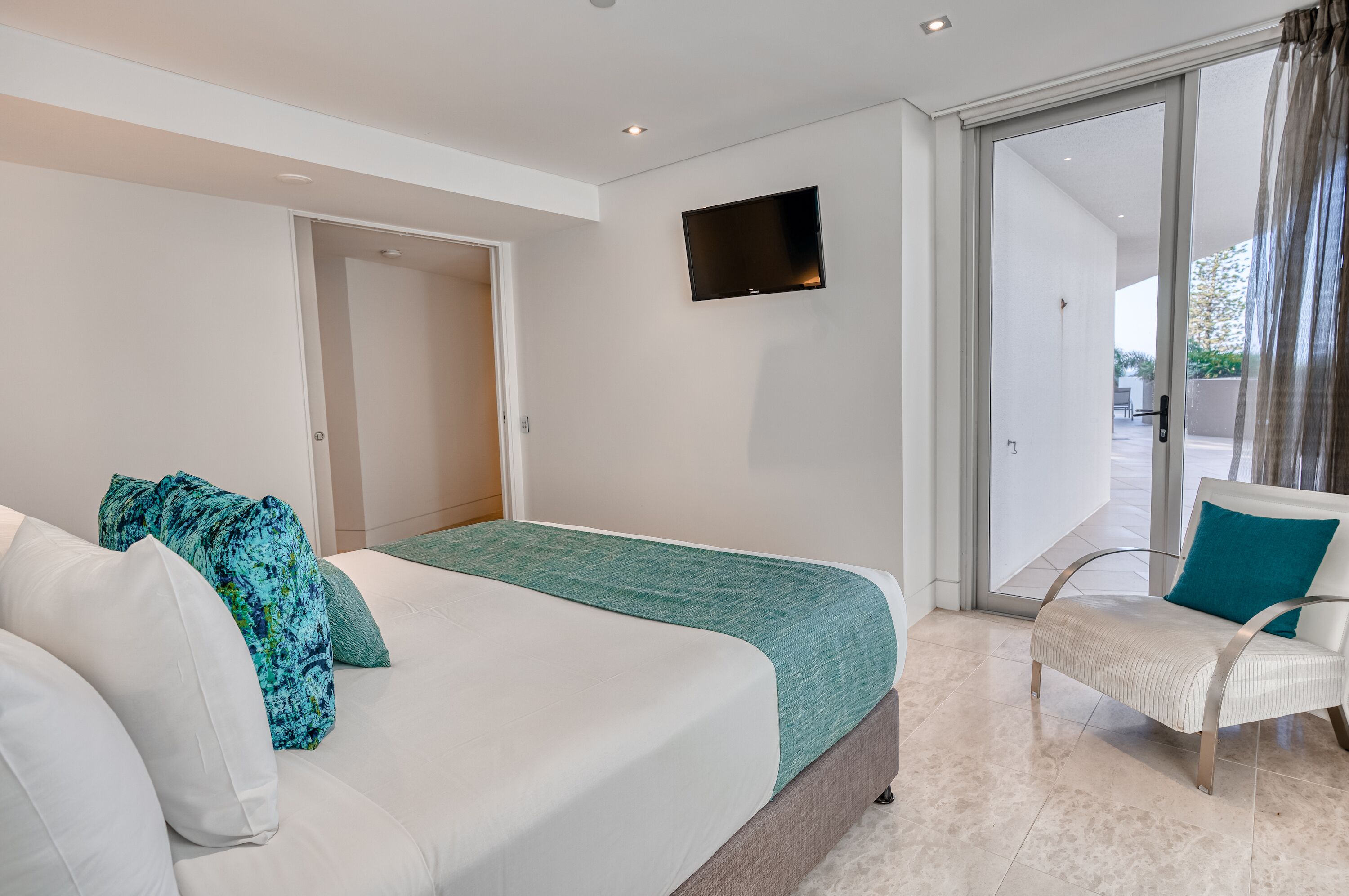 Et moderne hotelværelse med seng, stol, fjernsyn og en skydedør til en balkon.