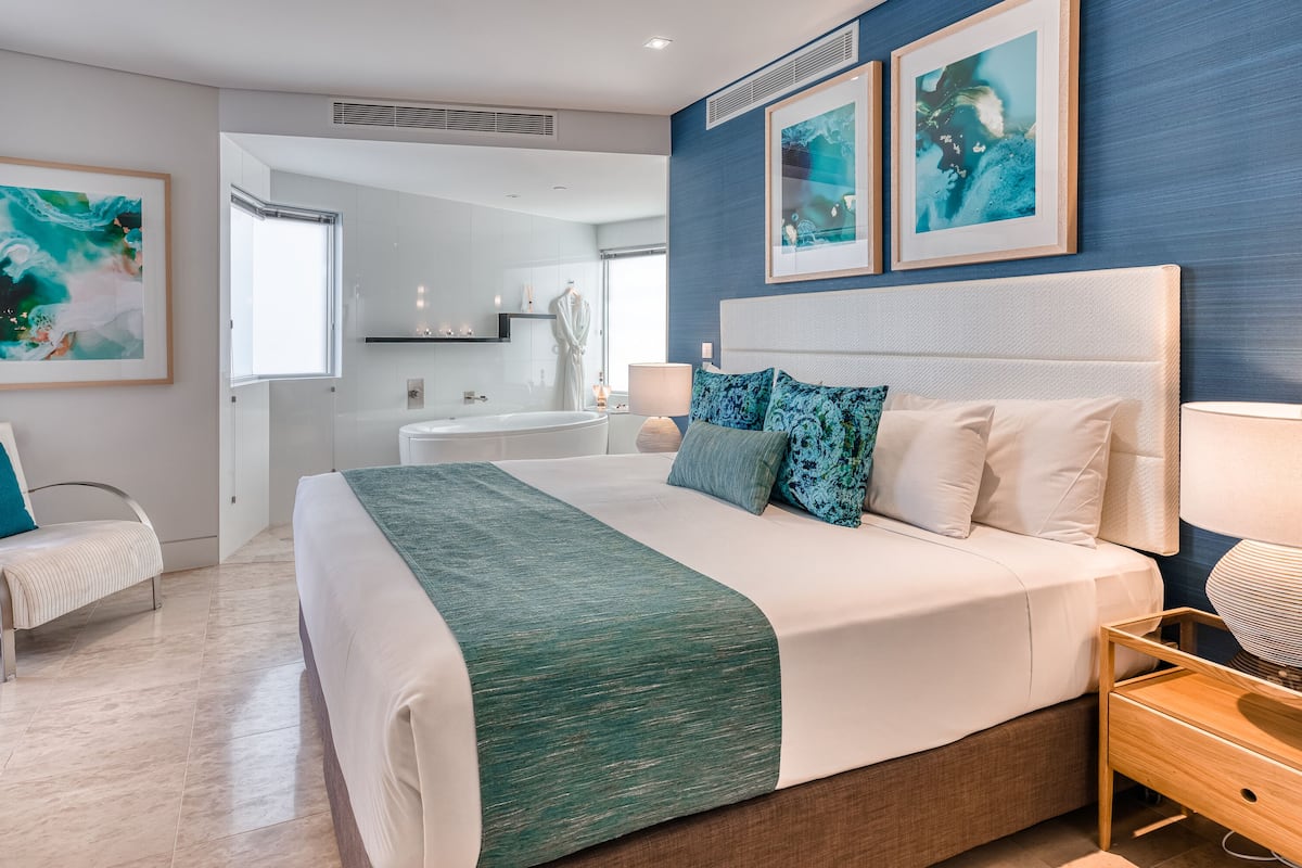 Una habitación de hotel moderna con una cama grande, una mesita de noche, una silla y vistas al baño.