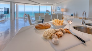 A modern kitchen with a large island, a view of the ocean, and a dining area with chairs and a table.