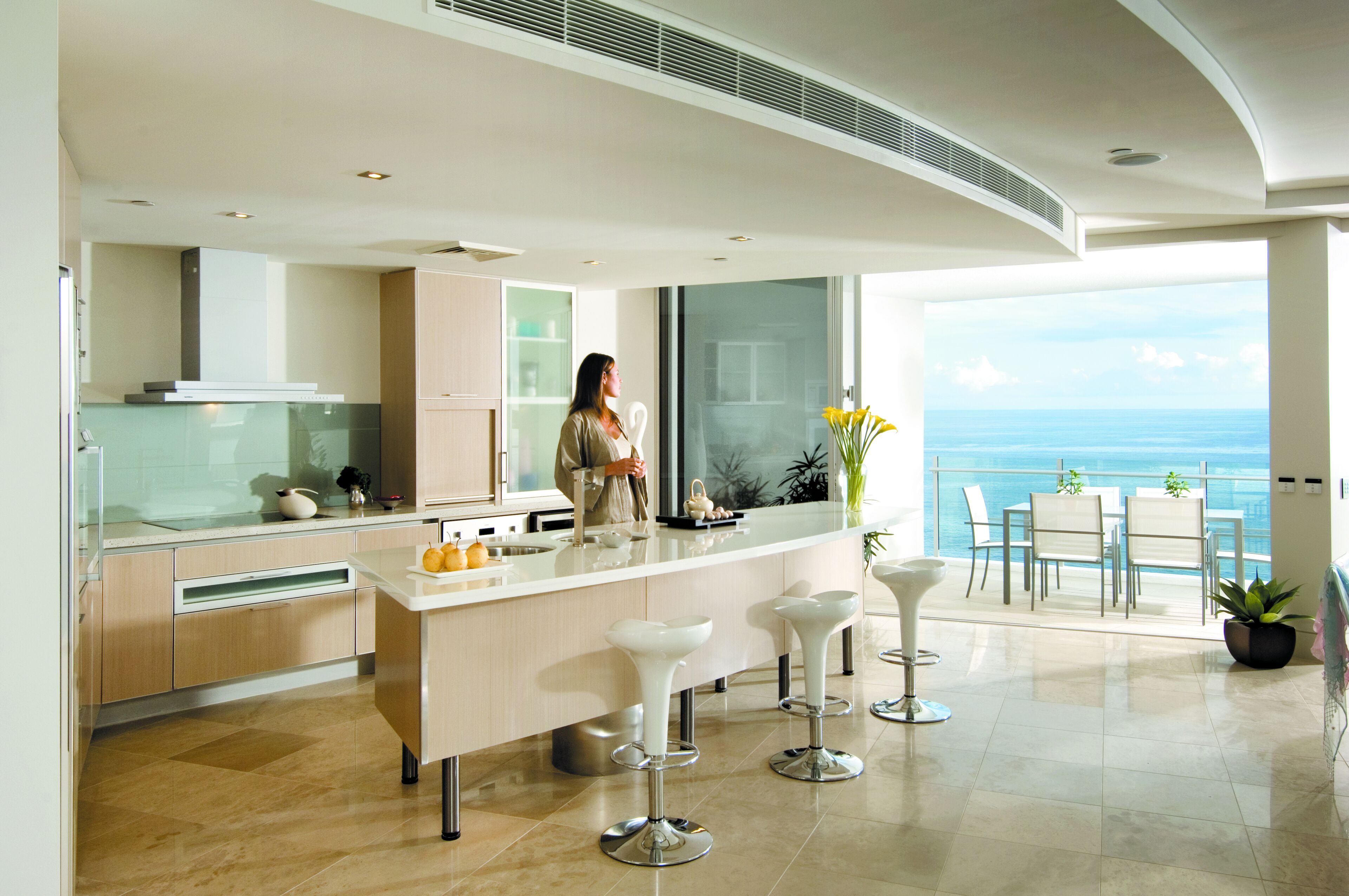 A modern kitchen with a large island, bar stools, and a view of the ocean.