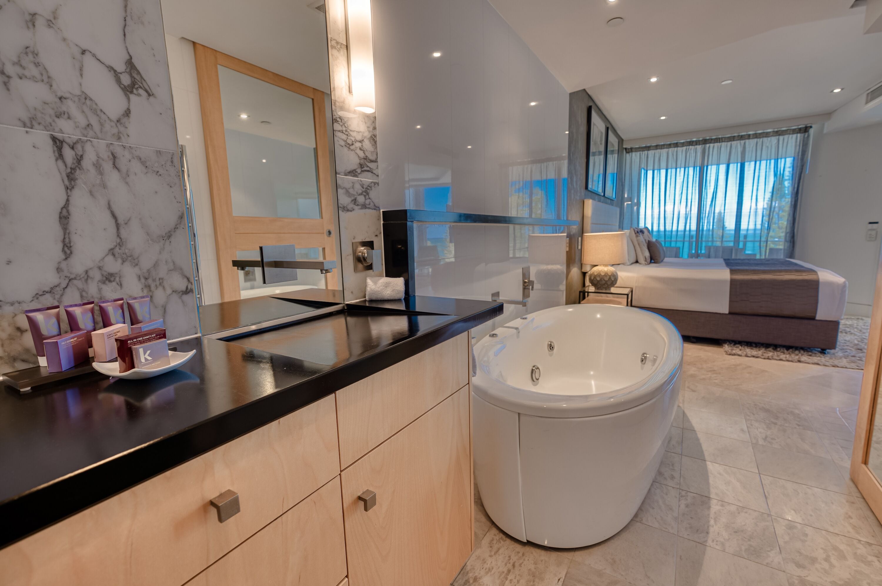 Un baño moderno con tocador de mármol, una bañera amplia y una cama con vistas.