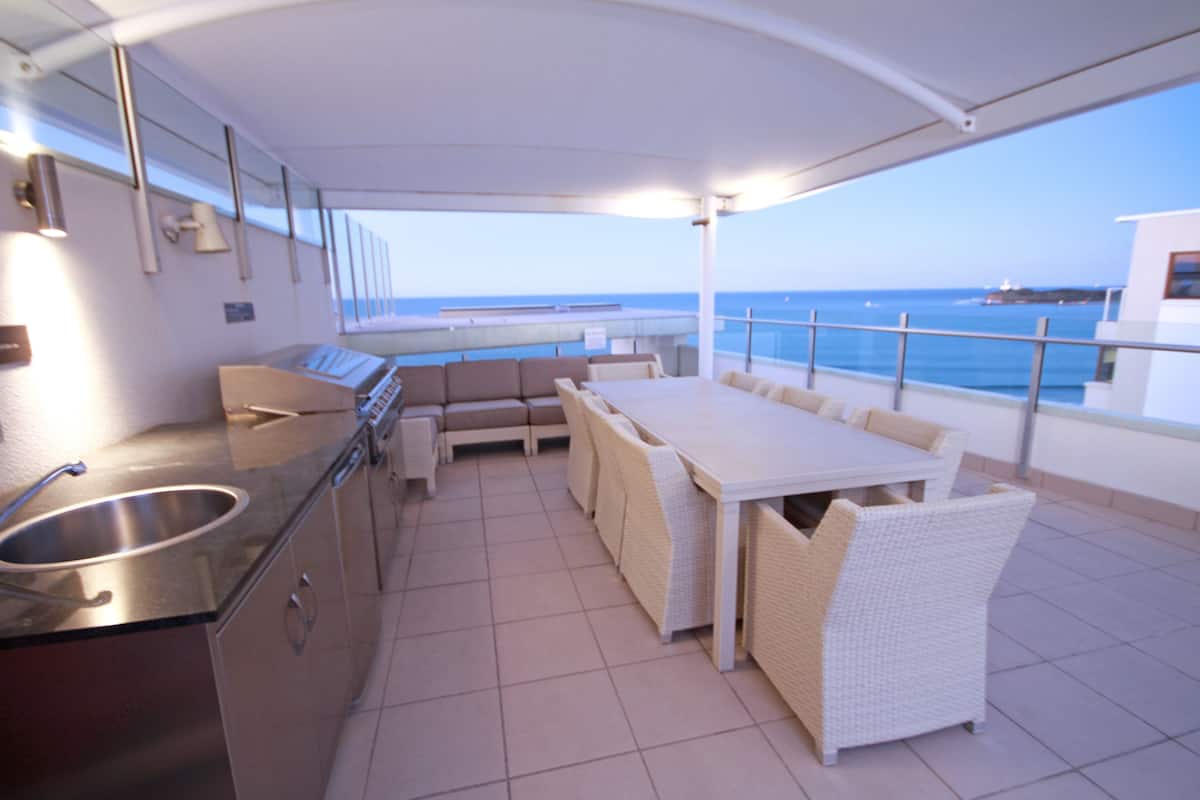 Un espacio exterior para comer con vistas al mar, una cocina con fregadero y un conjunto de asientos.